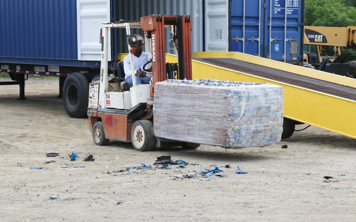 A forklift carrying a wrapped bale up a ramp into a shipping trailer